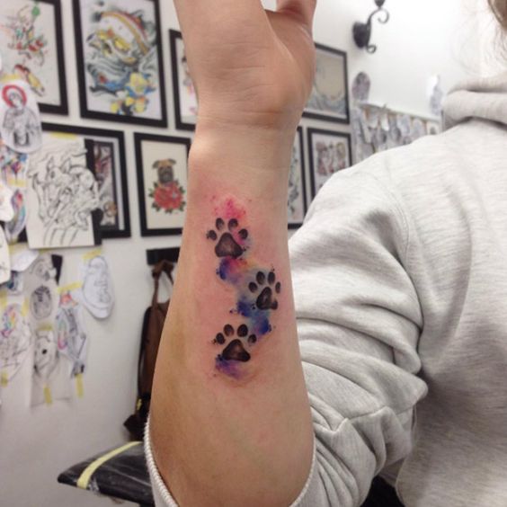 three black paw prints with colorful watercolor design tattoo on the wrist