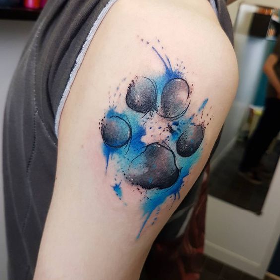 a large paw print with blue watercolor design tattoo on the shoulder of the man