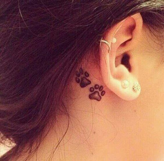 two small paw prints on the back of the woman's ear tattoo
