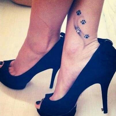 four small paw prints tattoo on the ankle of the woman in heels