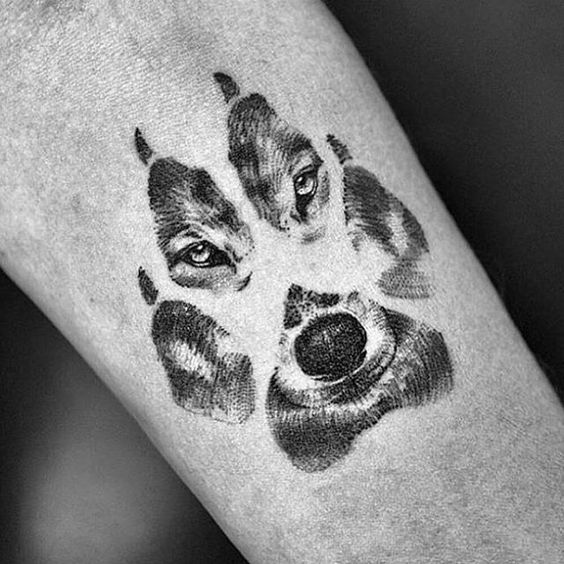 a large paw print with the face of a husky tattoo on the forearm