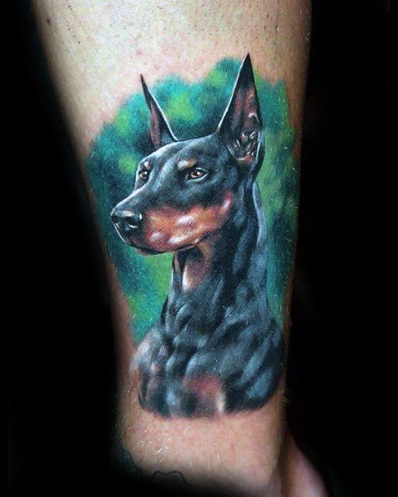 realistic Doberman looking sideways with a green background tattoo on the leg