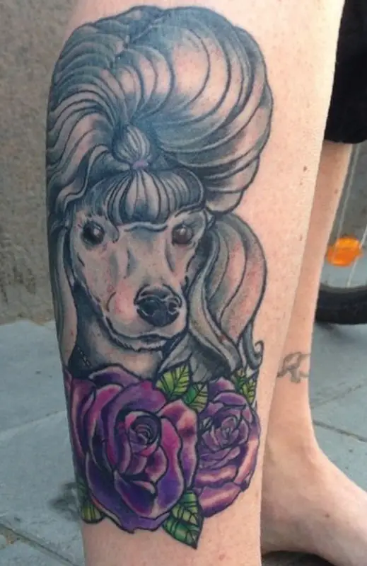 A stylish gray Poofdle with purple flowers and green leaves tattoo on the leg