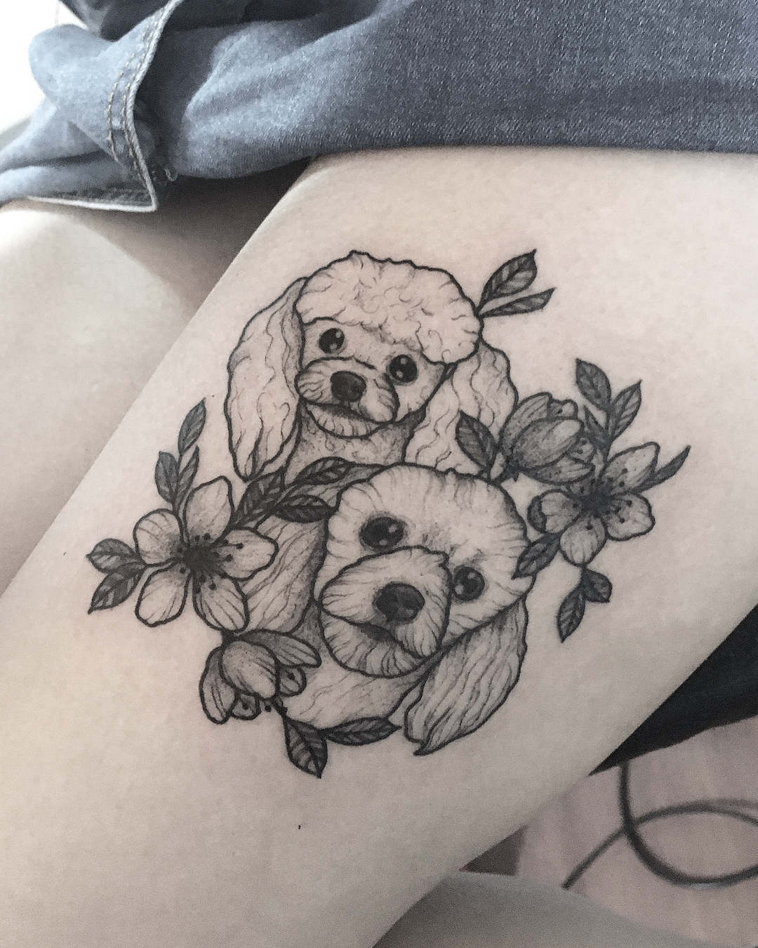 two outline faces of Poodle puppy with flowers tattoo on the thigh