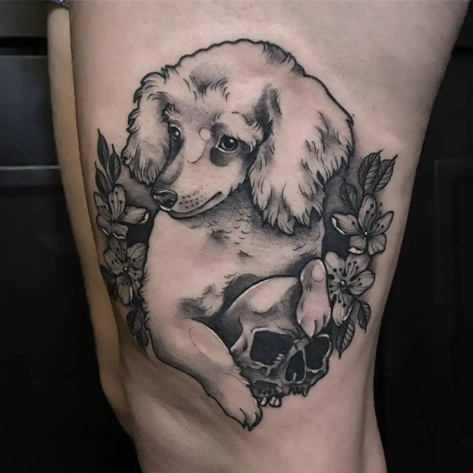 A black and gray poodle with flowers and leaves tattoo on the thigh