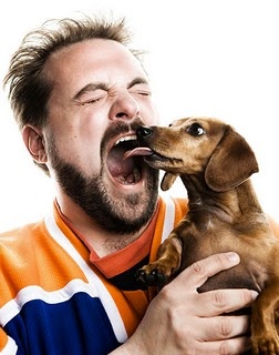 Kevin Smith opening his mouth while his dog is licking him
