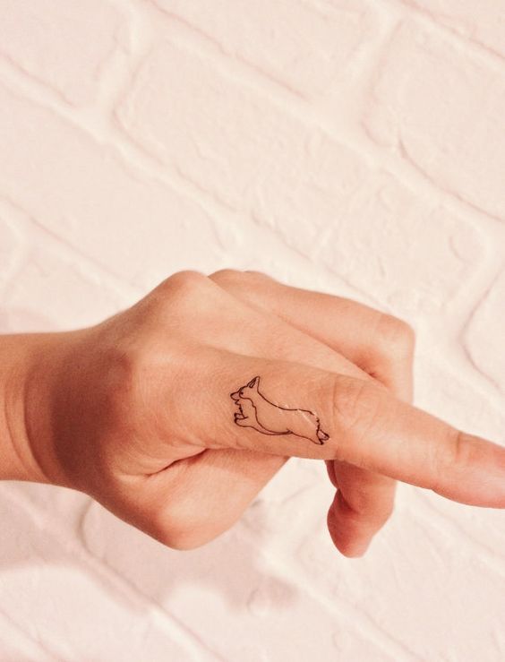 An outline Corgi tattoo on the finger of a woman