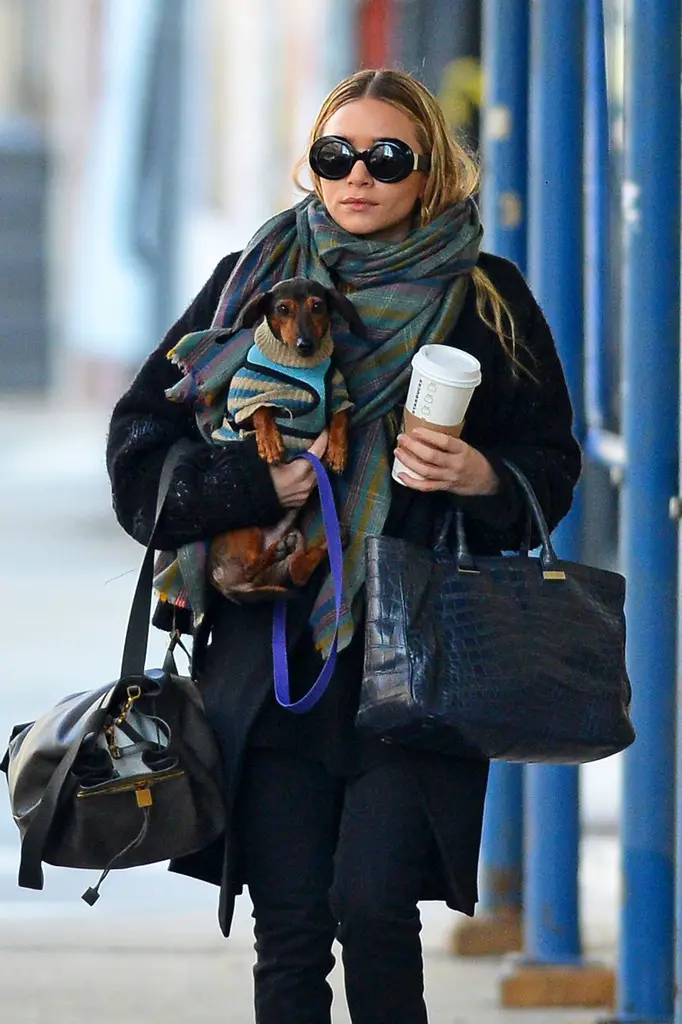 Ashley Olsen walking in the street while carrying her coffee, bags and her Dachshund