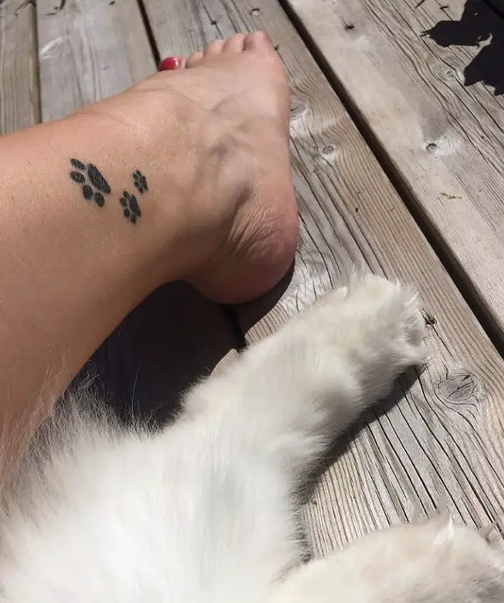 three paw prints tattoo on the leg of the woman next to the legs of her white dog
