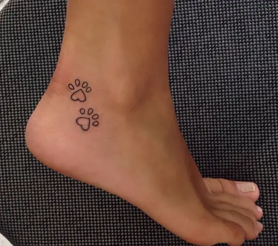 outline of two paw prints tattoo on the heel of the woman