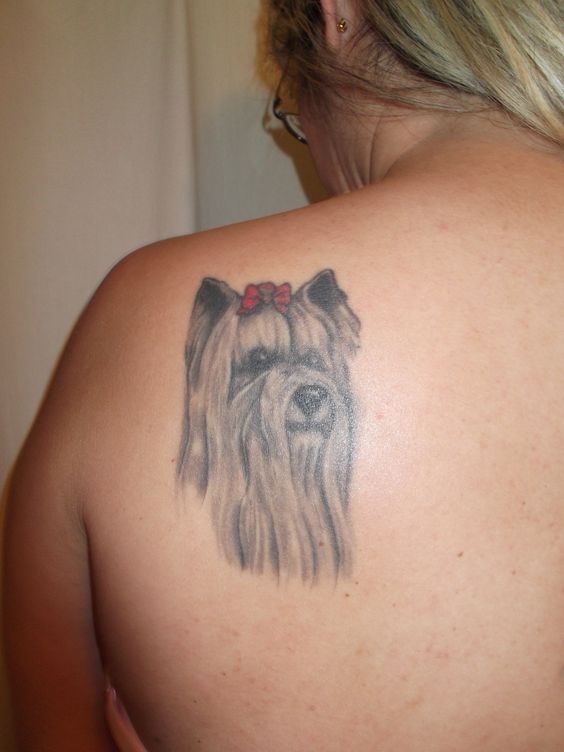 black and gray long haired yorkie with a red ribbon on top of its head tattoo on the back