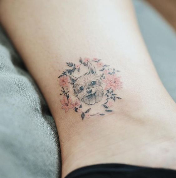 a happy yorkie inside a pink floral circle frame tattoo on the ankle