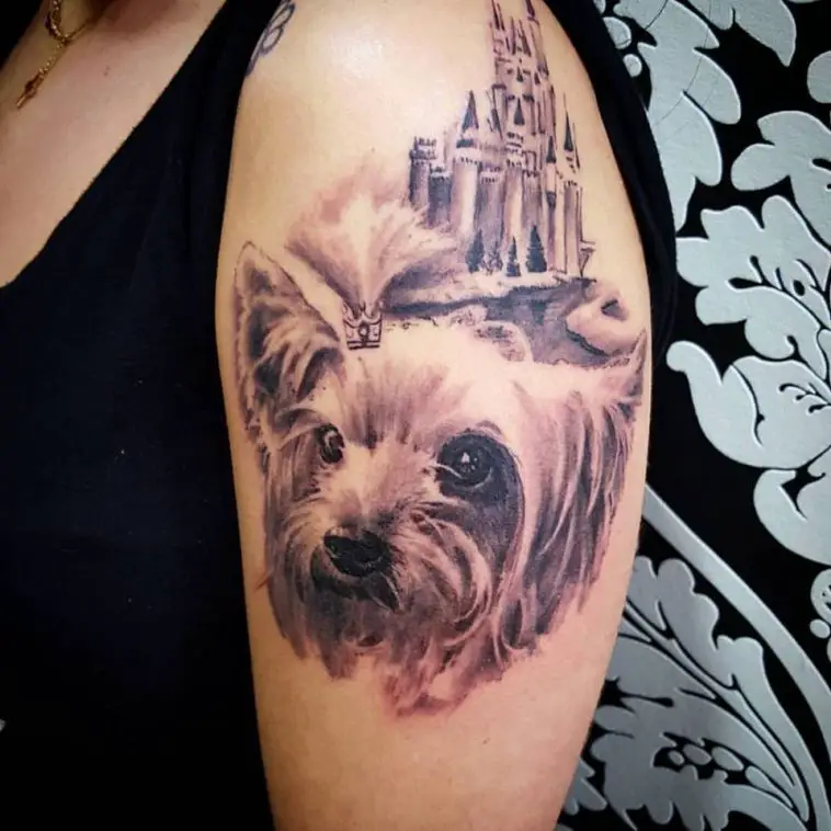 a black and gray yorkie with a castle behind her tattoo on the shoulder of the woman