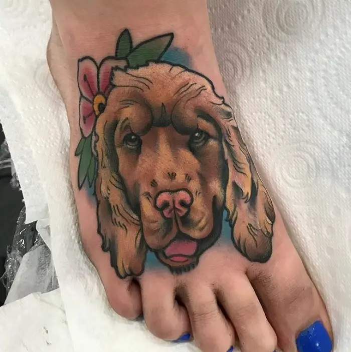 animated face of Cocker Spaniel with flowers and leaves tattoo on the foot