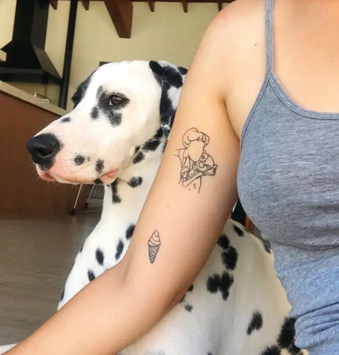 an outline of a girl hugging a Dalmatian dog tattoo on a girls biceps near the armpit while her Dalmatian dog is sitting behind her