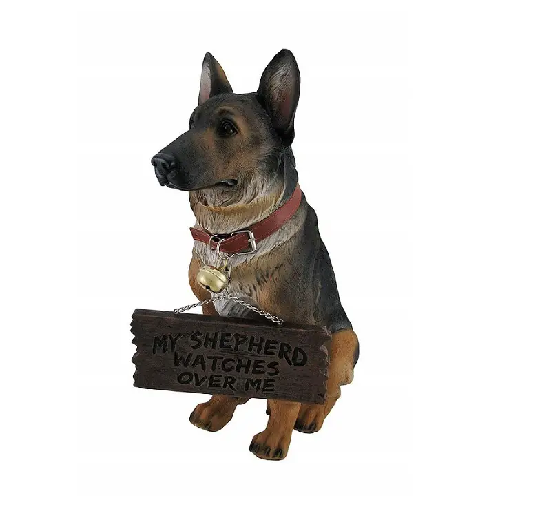 A statue of a german shepherd wearing a sign that says - My shepherd watches over me