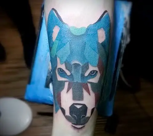 artistic face of a Husky with blue, green, red, and black colors tattoo on the forearm of a man