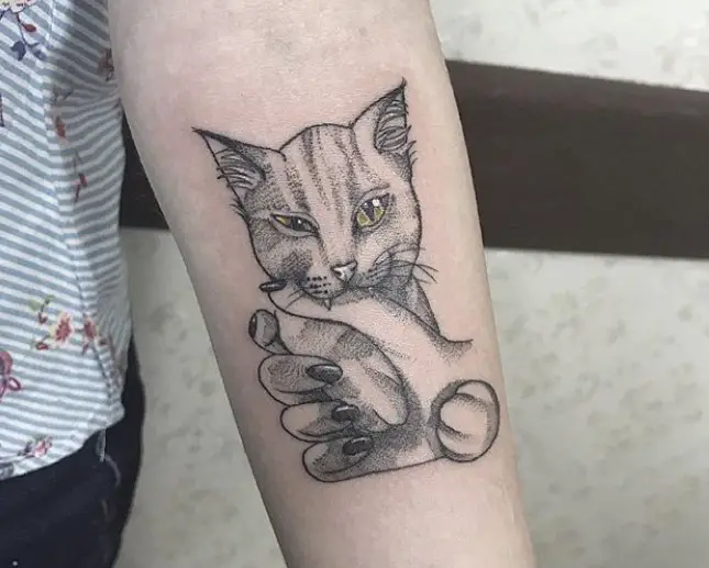 A black and gray cat with a hand of a woman tattoo on the forearm
