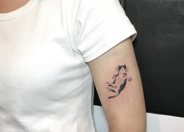 A small lying on its back Black and White Cat tattoo on the shoulder