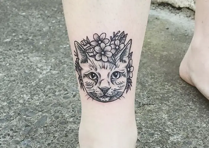 face of a cat with flowers and leaves tattoo on the leg