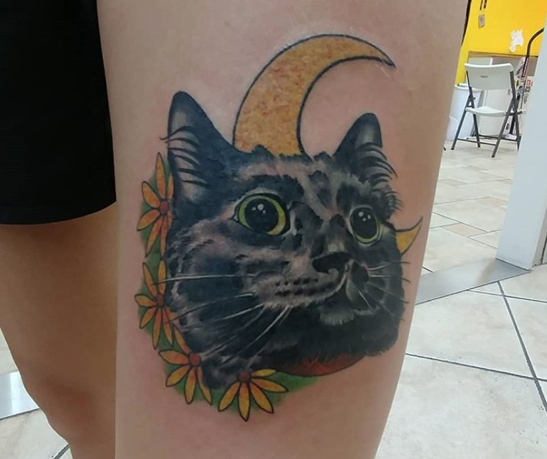 face of black cat with flowers and crescent moon behind it tattoo on wrist