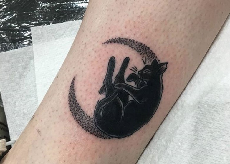 black cat leaning on a crescent moon while licking its hands