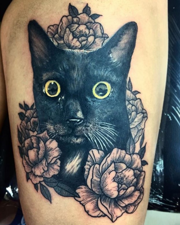 a large face of black cat with flowers around it tattoo