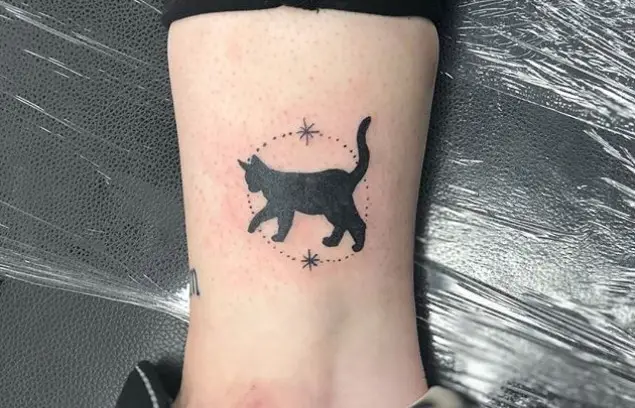 walking black cat inside a dotted circle with stars tattoo on legs