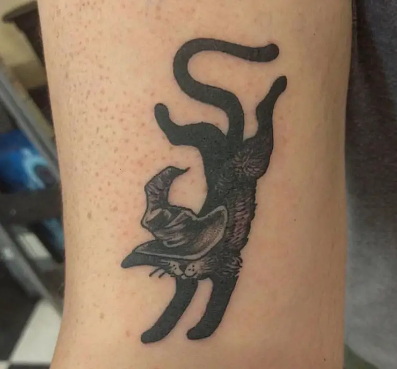 falling black cat wearing a hat tattoo on wirst