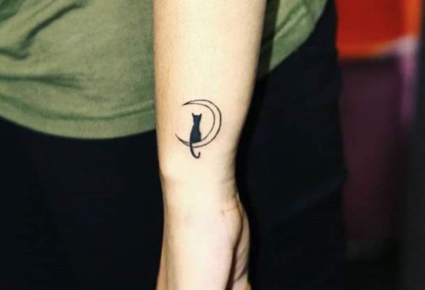 small tattoo on the forearm of a black cat sitting on a crescent moon