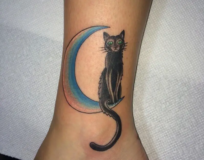 black cat sitting on the blue green and peach colored crescent moon tattoo on the ankle