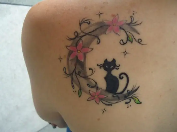 black cat sitting on a crescent moon with flowers tattoo on the back