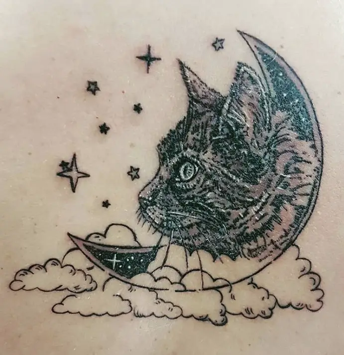 face of a cat in a crescent moon with clouds and stars tattoo