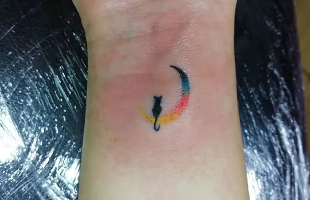 black cat sitting on the sunset yellow pink blue and black colored crescent moon tattoo on the wrist