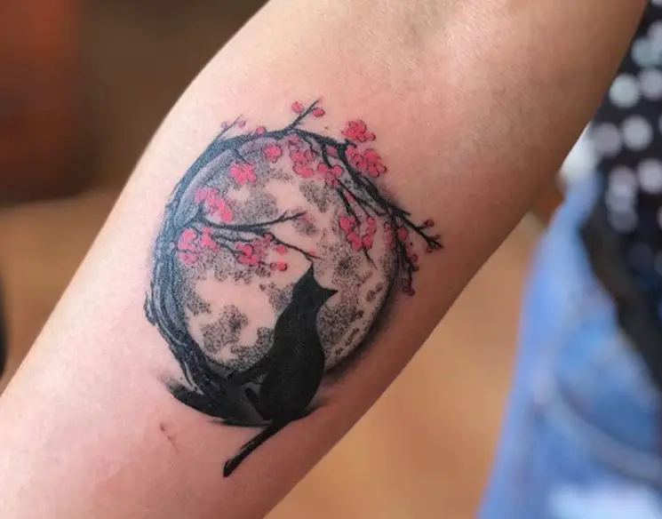 black cat and a moon with sakura flowers tattoo on the forearm