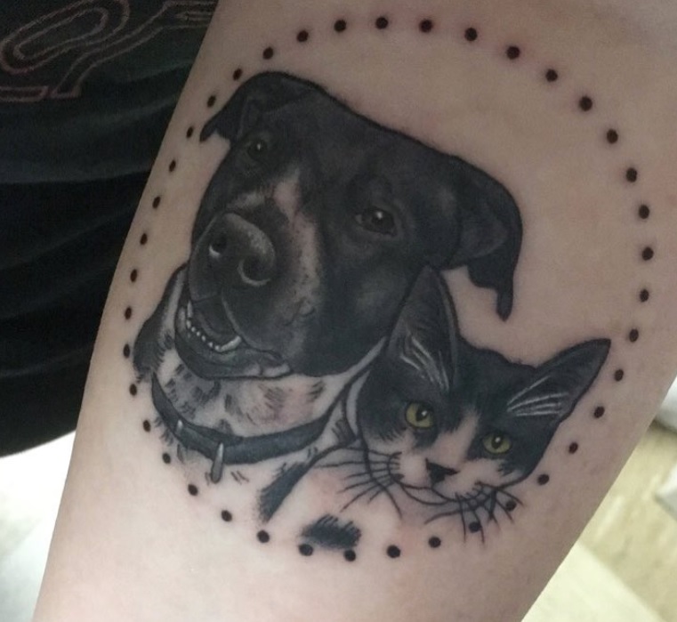 faces of dog and cat inside a dotted circle tattoo on the arm