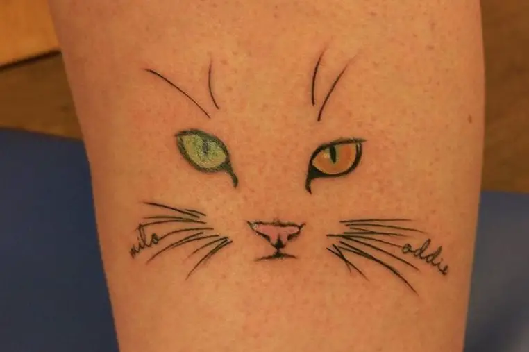 minimalist face of a cat with orange and green eyes tattoo on the leg