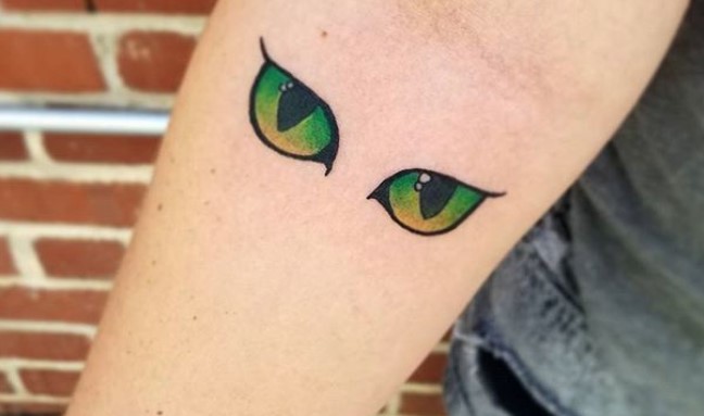 green and yellow eyes of a cat tattoo on the forearm