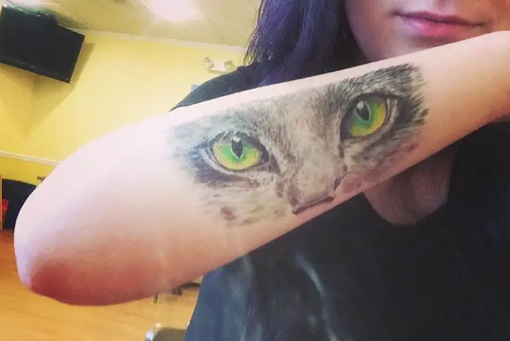 eyes and nose of a cat tattoo on the arm of a girl