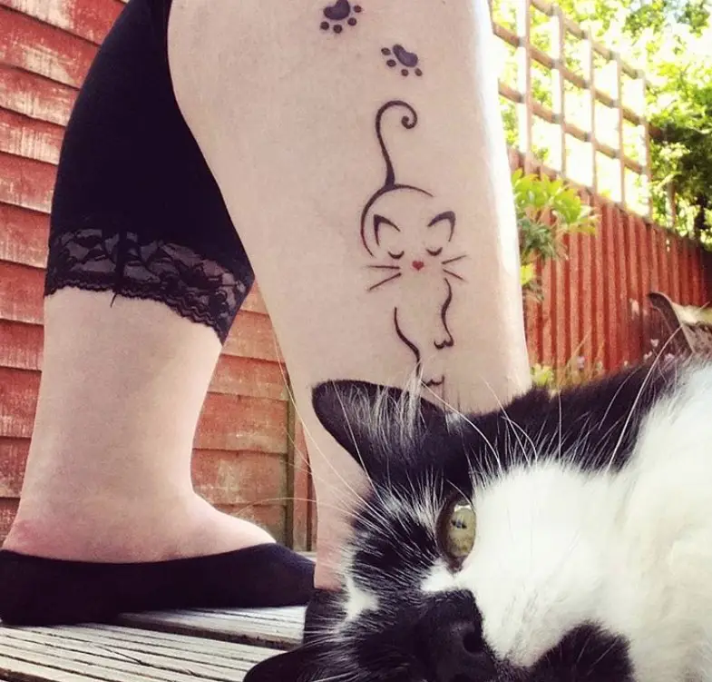 face of a cat lying down on the floor behind the leg of girl with a cat outline tattoo