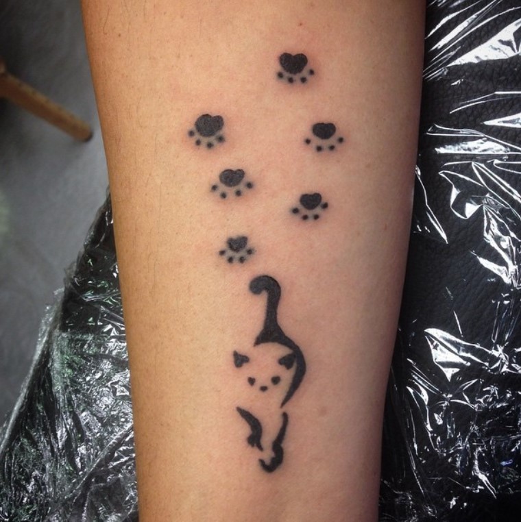 outline of cat with six Cat Paw Prints behind it tattoo on the forearm