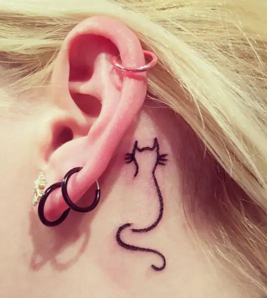 outline of a sitting on its back cat tattoo behind the ear of a girl