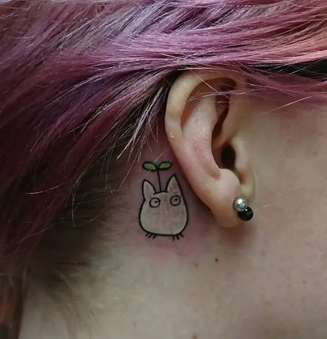 chibi totoro tattoo behind the ear of a woman with purple hair
