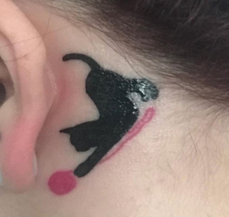 a black cat chasing a red yarn ball tattoo behind the ear of a girl