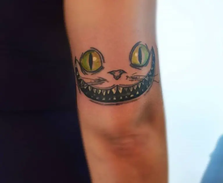 simple Cheshire Cat with green eyes tattoo on above the elbow