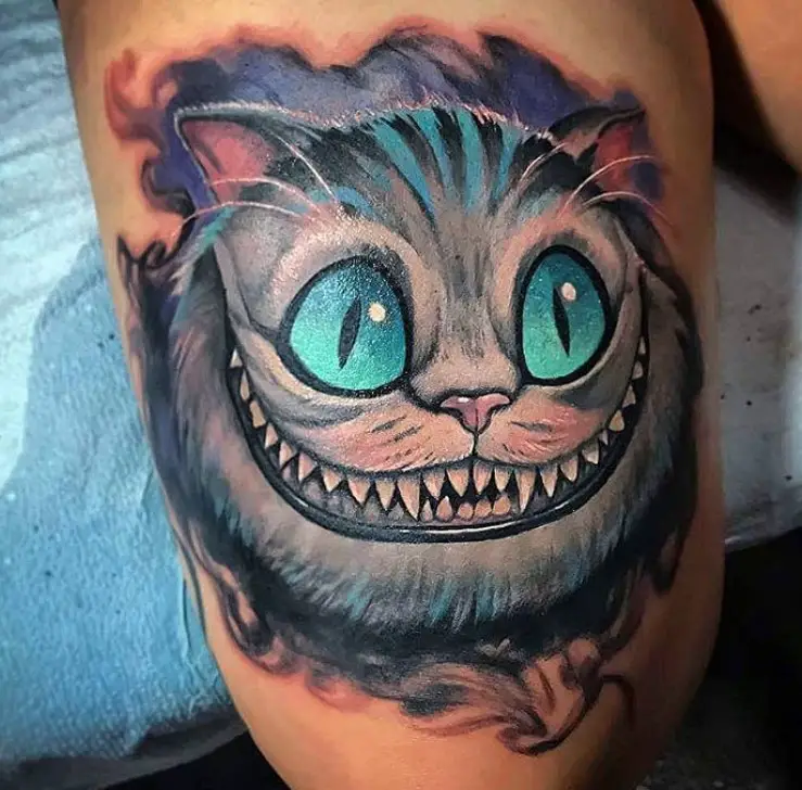 gray Cheshire Cat with aqua blue eyes and blue line on its fur, in a blue and black smoky shadow tattoo on the leg