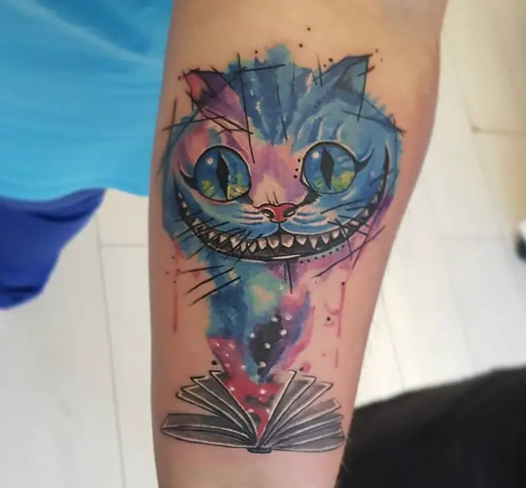 blue, pink, purple and red watercolor Cheshire Cat smoke coming from a book tattoo on the forearm