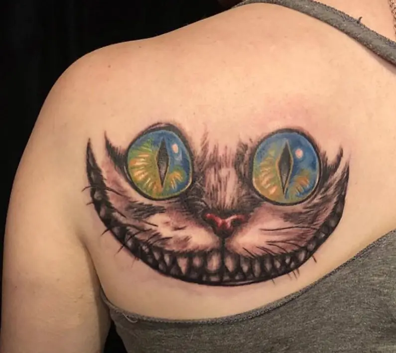 gray and black Cheshire Cat with yellow and blue eyes and red nose tattoo on the back