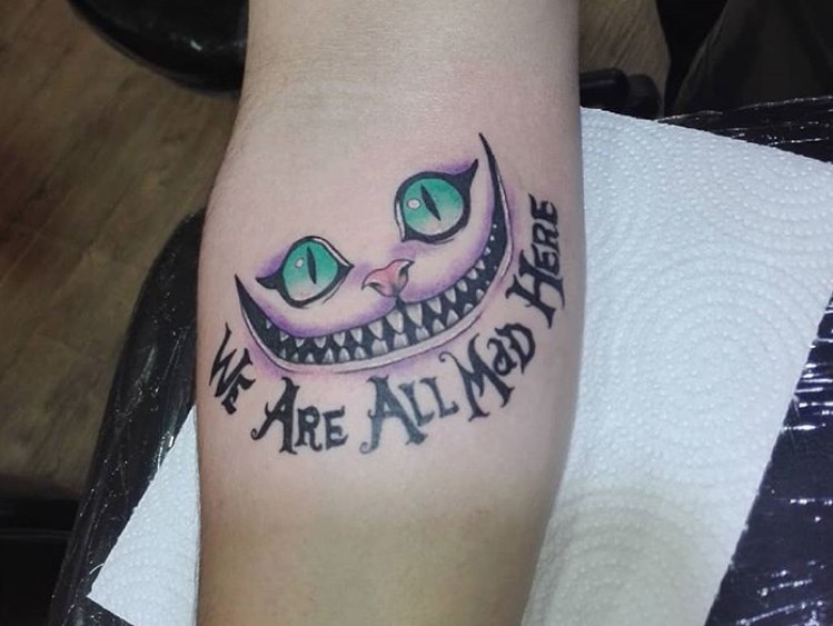 simple purple Cheshire Cat with pink nose and green grass with words