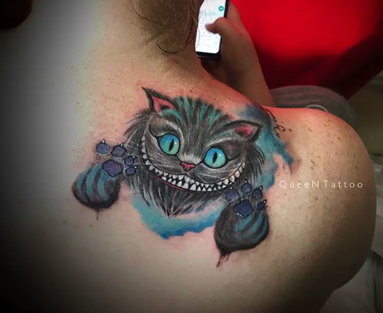 black Cheshire Cat with aqua blue eyes and lines of aqua blue colors in its fur with purple paws while floating in a blue watercolor smoke tattoo on the shoulder